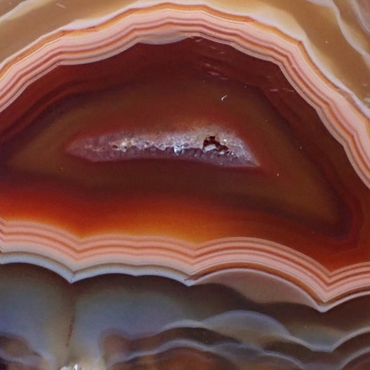 Close up of a Malawi candy agate showing outer ghost banding with peach bands around a red centre with a small crystalline centre within