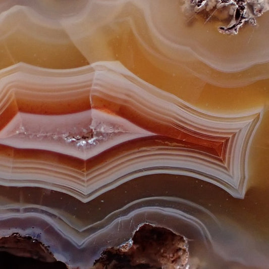 A close-up of a drusy centre of a candy malawi agate banded with shades of red and orange to yellow