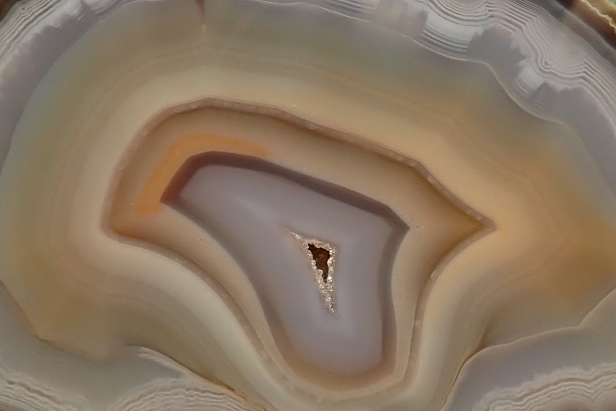 Ghost Mountain agate 80 mm – banding detail, smooth concentric arcs in cream and amber-orange with sparkling drusy vug, hand-polished