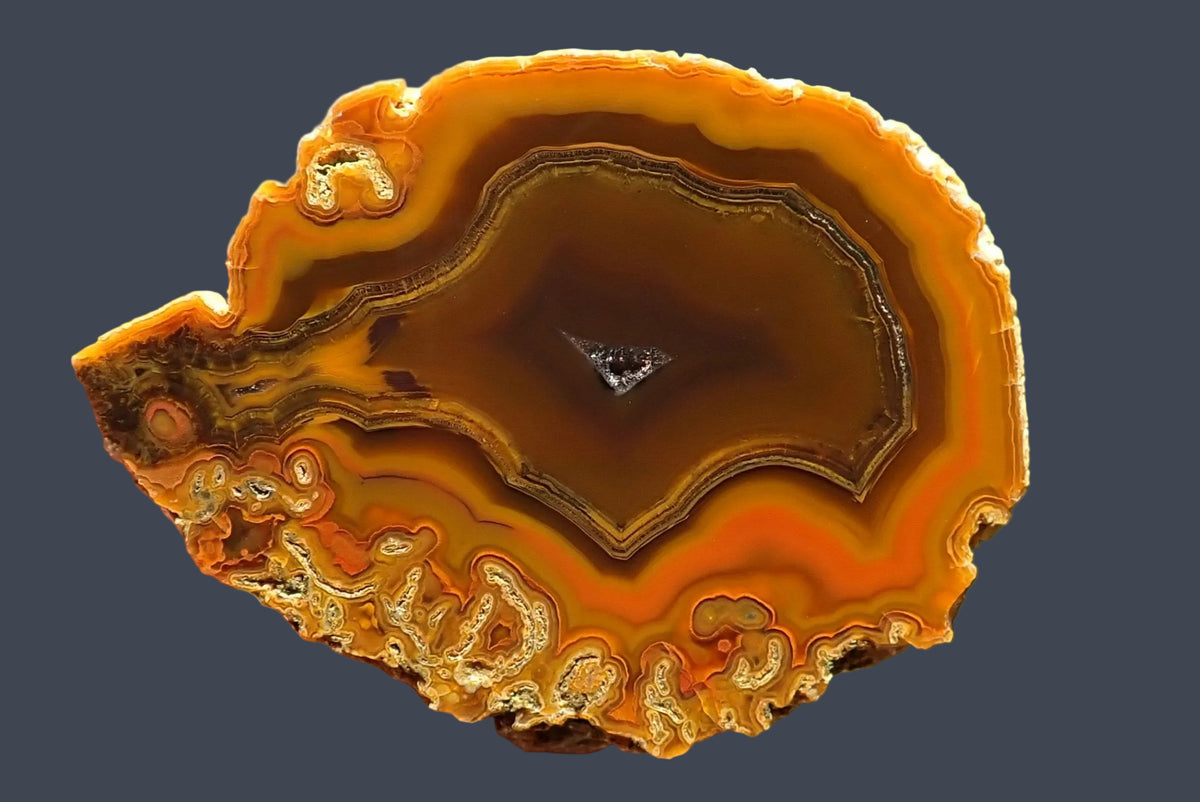 Lilangabi agate 68 mm – hand-lapped face with angular fortification banding, chromatography in golden yellow, orange and brown, moss inclusions along the lower edge and a small central drusy vug.