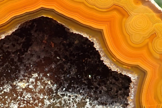 Lilangabi agate 74 mm, close-up of very fine angular fortification banding around the crystal-lined drusy vug, showing golden-yellow, amber and brown bands with white crystal highlights.