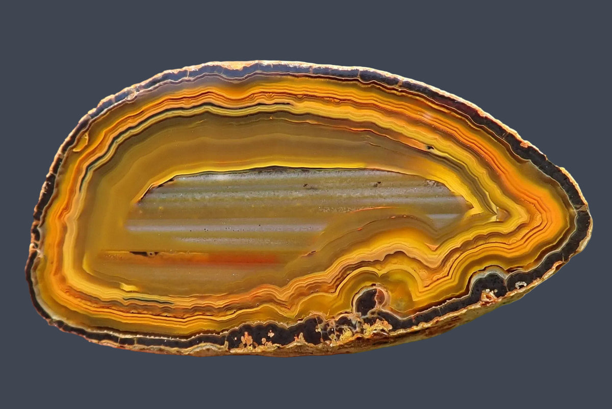 Lilangabi agate 60 mm, hand-lapped face with pale grey horizontal waterlines across an amber centre, surrounded by golden yellow and orange fortification bands with dark outlines and scalloped lower banding