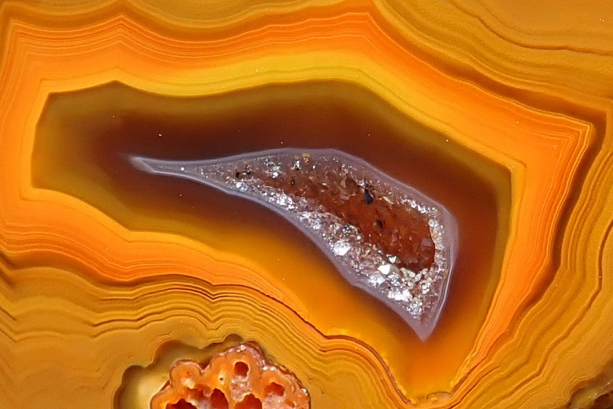 Lilangabi agate 49 mm, detail of the drusy vug with a pale grey rim and visible crystals, enclosed by dark brown, orange and golden-yellow fortification bands.