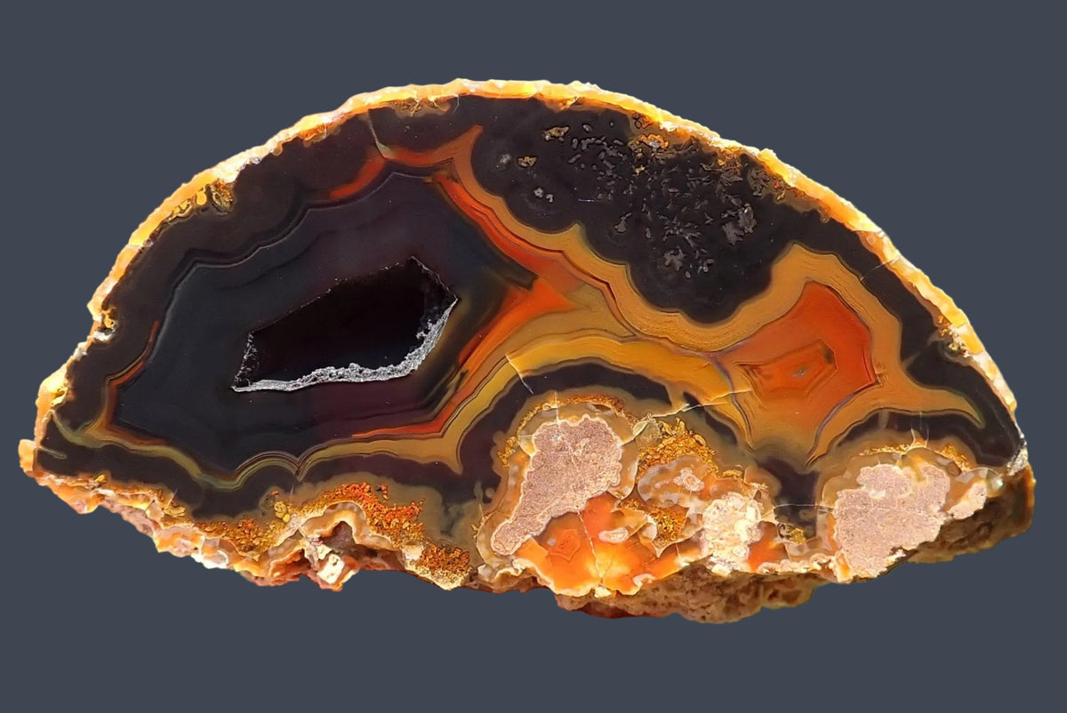 Lilangabi agate 71 mm, hand-lapped face with an open vug and angular fortification banding in charcoal, muted purple, orange and golden yellow, Lebombo Mountains.