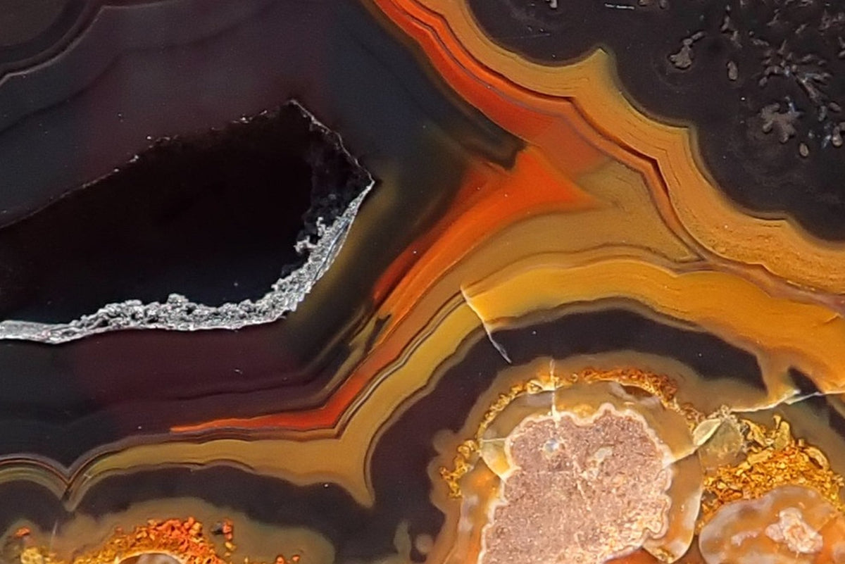 Lilangabi agate 71 mm, detail of the open vug and surrounding fortification bands, with charcoal-purple layers bordered by orange and golden yellow.