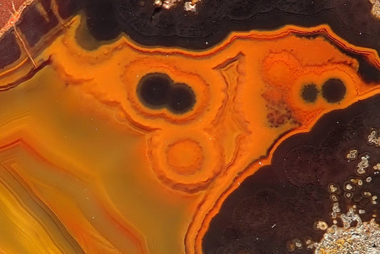 Lilangabi agate 63 mm – detail of paired dark eyes and rounded orange bands forming face-like pareidolia, bordered by fine orange and gold fortification bands.