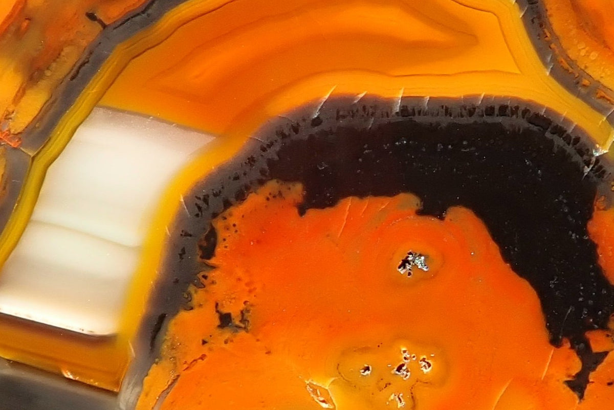 Lilangabi agate 60 mm – detail of cream-white waterline layers bordered by yellow and charcoal-grey bands, contrasting with the vivid orange centre and orange-gold upper banding.