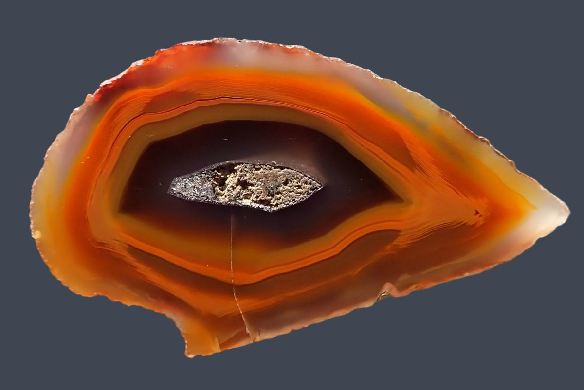 Lilangabi agate 68 mm – full hand-lapped face with broad concentric bands narrowing to a point, chromatography in orange and amber, and a central drusy vug surrounded by deep reddish brown.