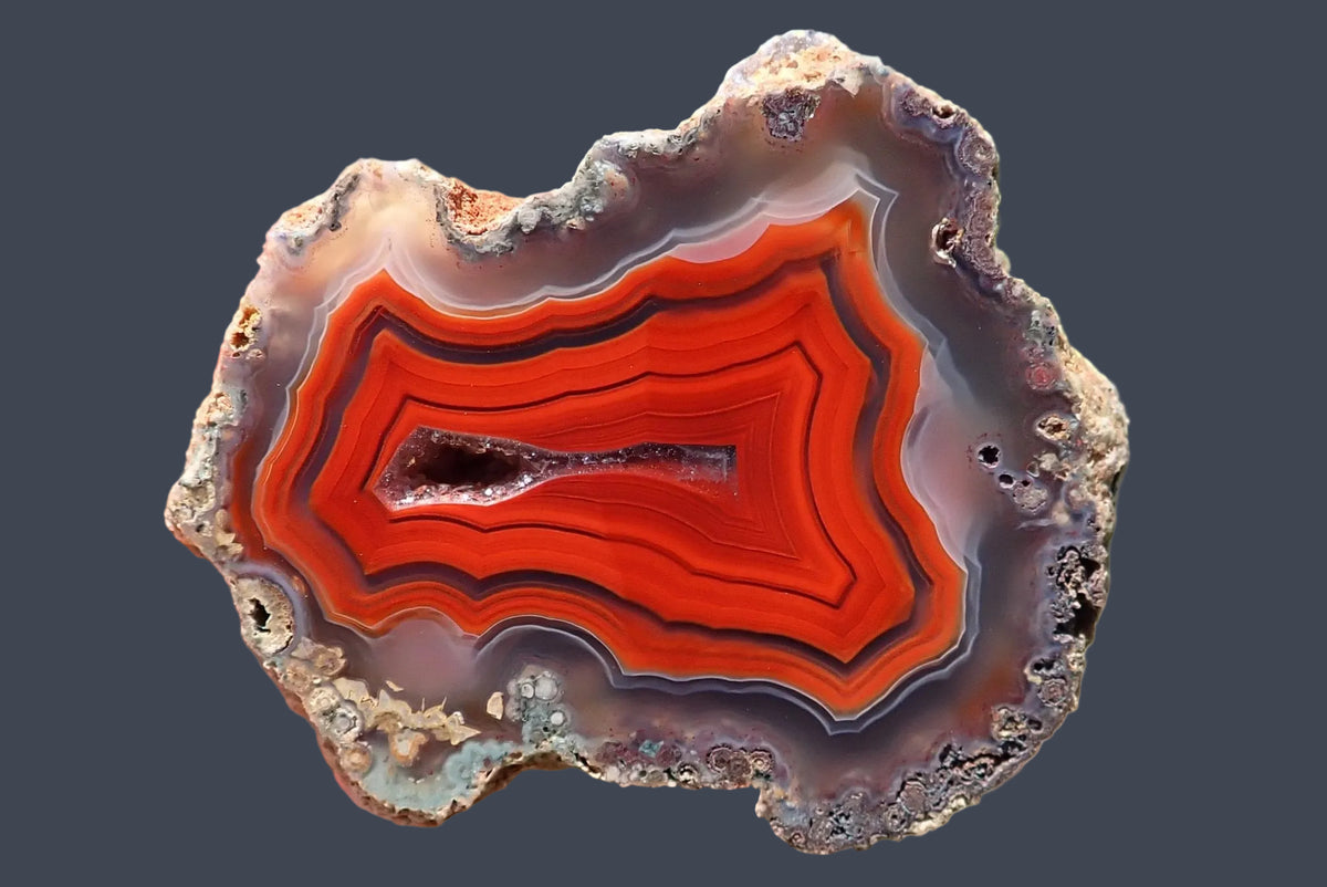Malawi agate 42 mm, hand-polished face with red-orange fortification banding, grey-purple outer ghost bands and an elongated central drusy vug, Ngabu, Malawi.