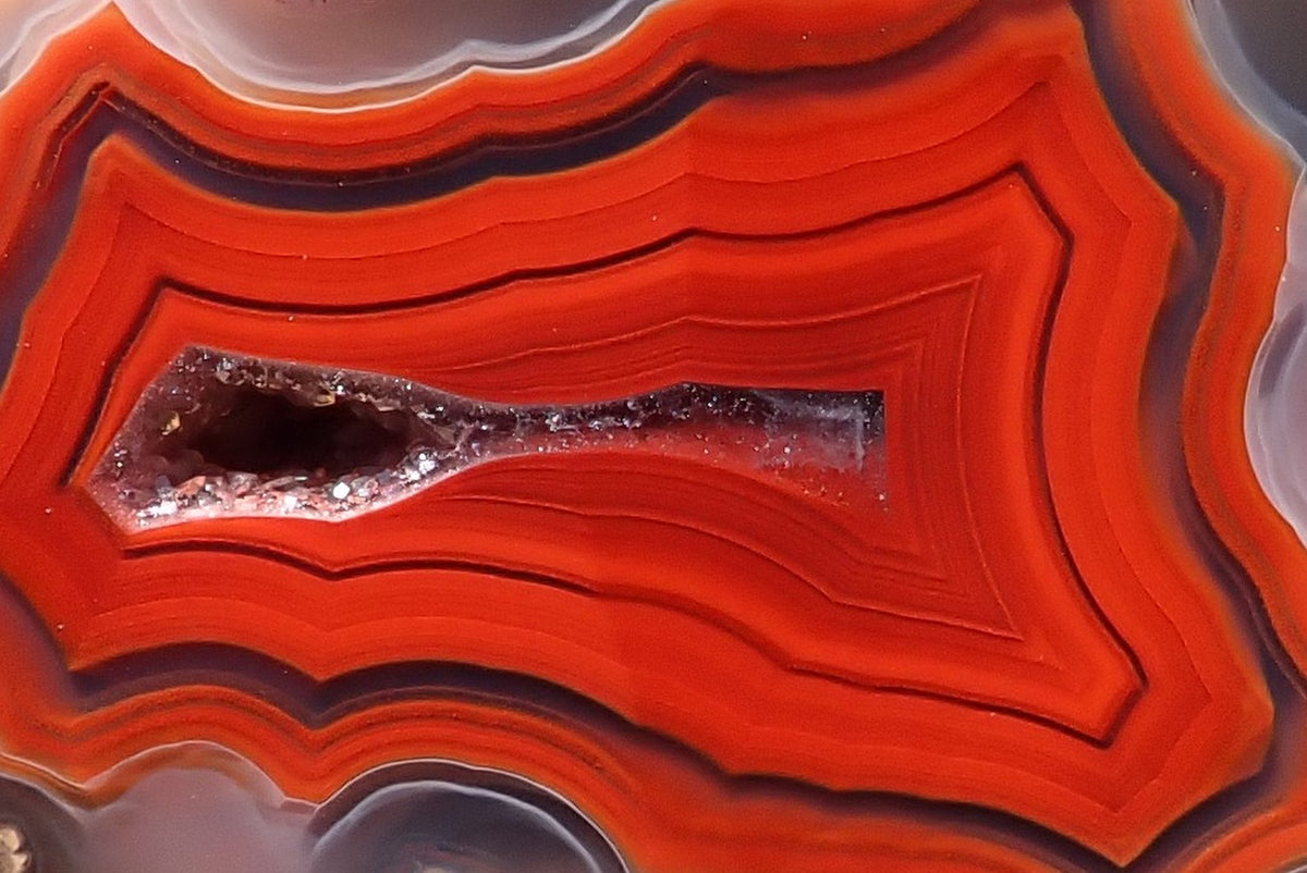 Malawi agate 42 mm, detail of the crystal-lined drusy vug surrounded by angular red-orange fortification bands and fine dark outlines, Ngabu, Malawi.