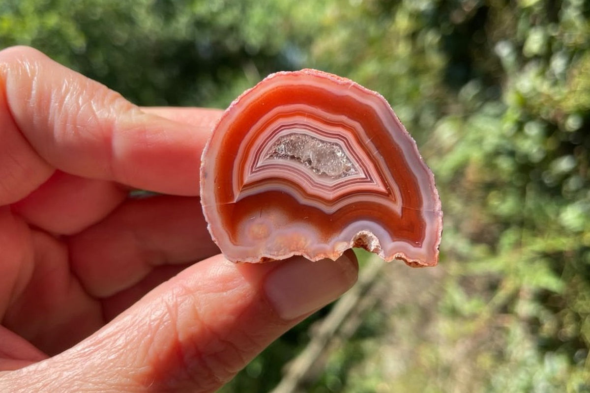 Malawi agate 38 mm – held for scale, showing red-orange outer bands, pale pink and white fortification banding and the crystalline drusy centre, Ngabu.
