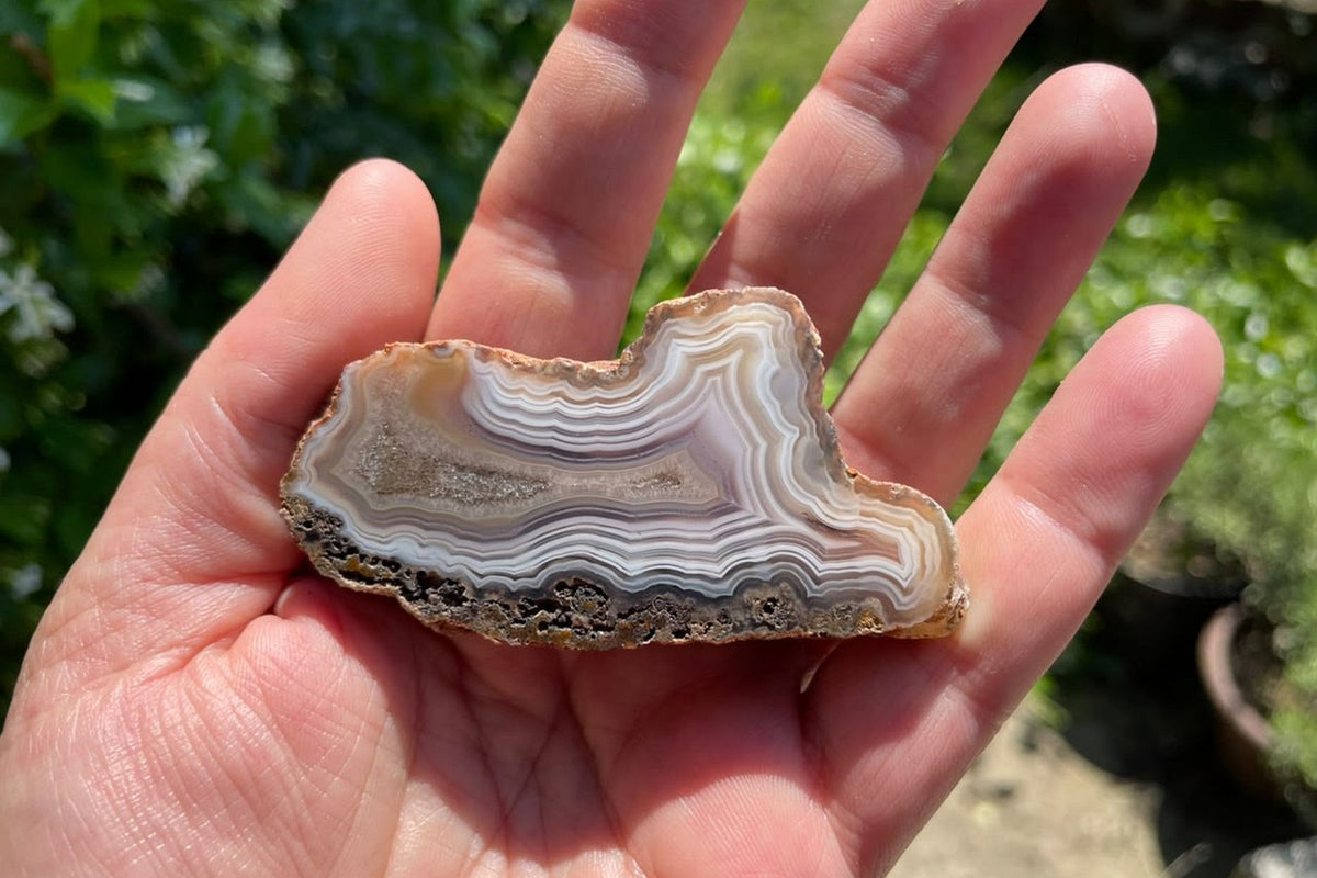 Malawi agate 70 mm resting in a palm for scale, showing its banded polished face and elongated calcite-bearing crystalline centre, Ngabu, Malawi.