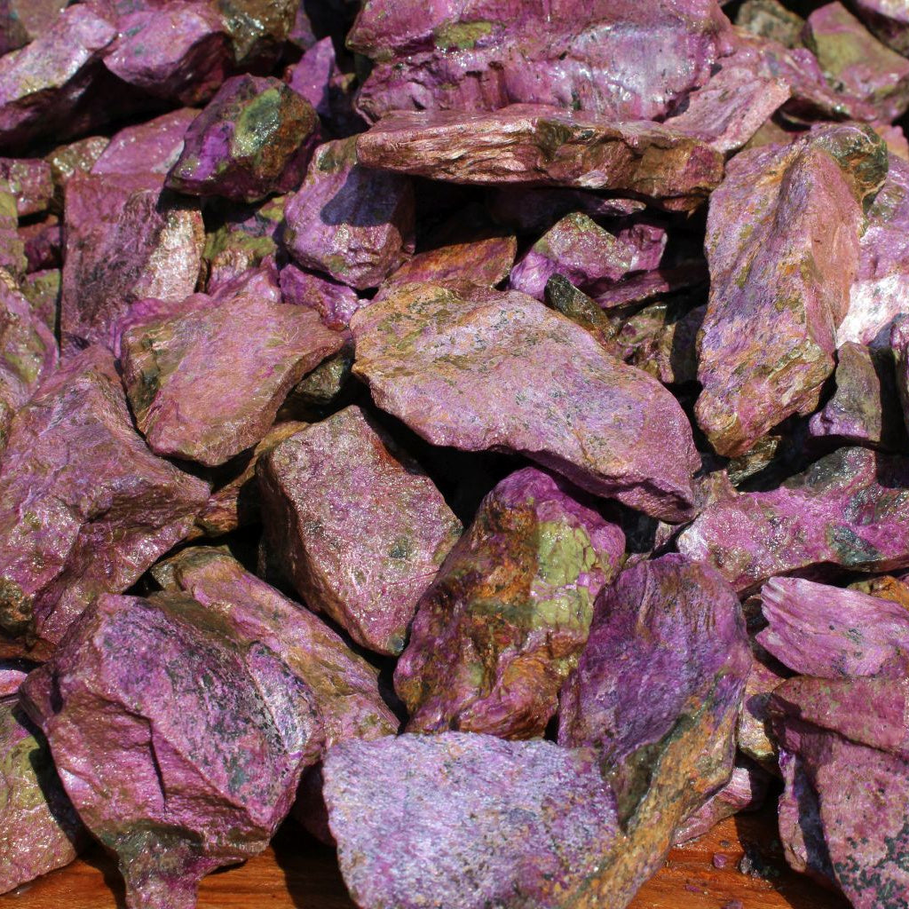 Wet natural stichtite specimen grade large rough in serpentine matrix, Kaapsehoop, South Africa — bulk pile showing lilac to purple tones and mixed sizes, wet finish | SKU STICHSPEC