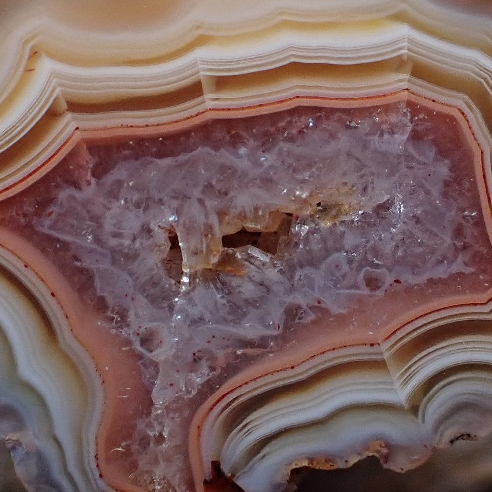 Close-up of Malawi agate 38 mm – open vug with macro-quartz crystals, rose-pink to lavender druzy halo, scalloped inner band edges and flow channel detail | SKU 000352