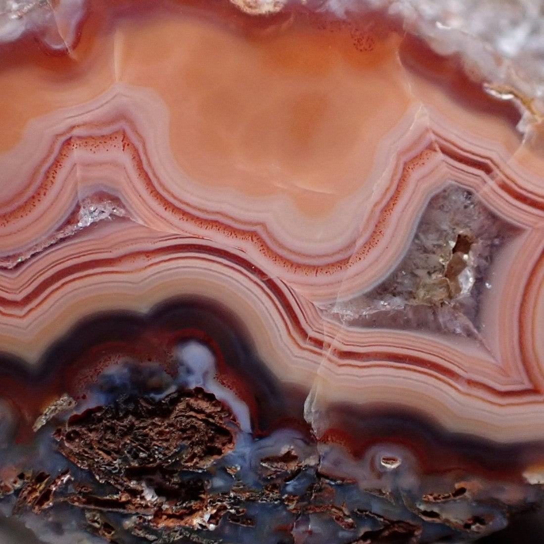 Close-up of Malawi agate 35 mm – carnelian-orange inner zone, wavy fortification banding, secondary inner zone with crystalline pocket, near-black lower band and blue-grey chalcedony accents | SKU 000359
