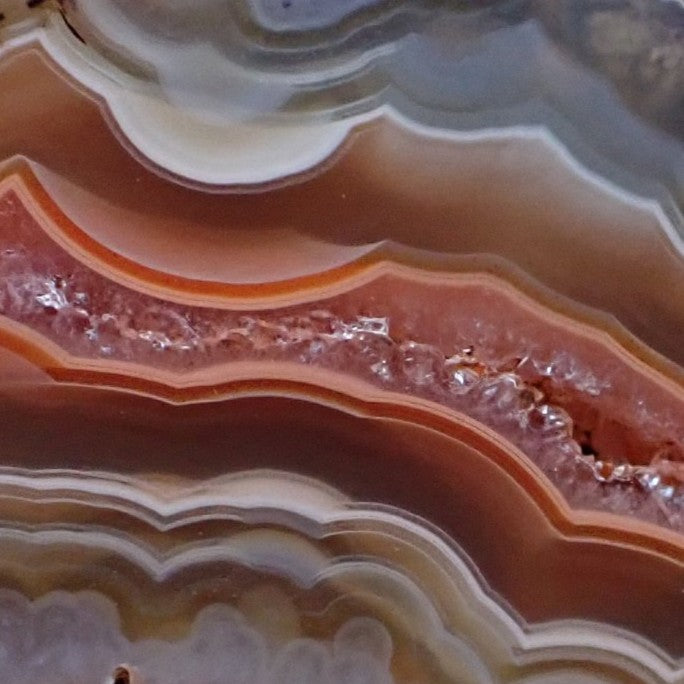 Close-up of Malawi agate 46 mm – elongated druzy quartz inner zone with thin orange framing band, scalloped sard-brown banding above and below, small open vug at lower-right margin | SKU 000370