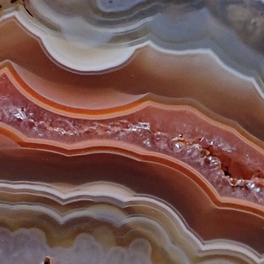 Close-up of Malawi agate 46 mm – elongated druzy quartz inner zone with thin orange framing band, scalloped sard-brown banding above and below, small open vug at lower-right margin | SKU 000370