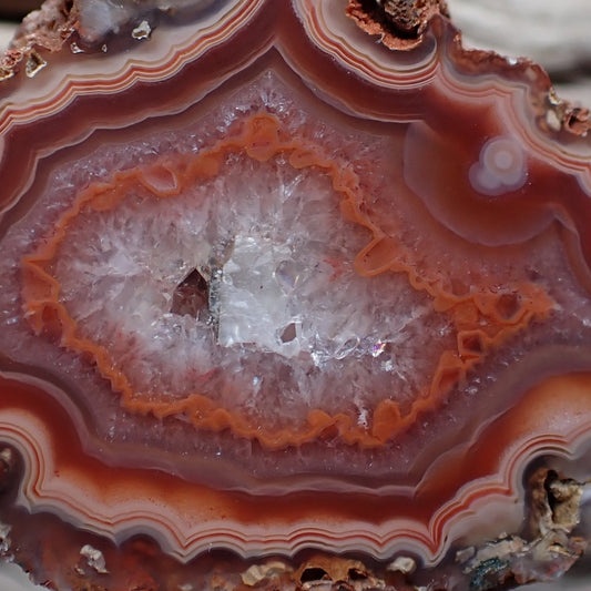 Close-up of a colorful Malawi agate with concentric layers of red, orange, and white around a drusy centre