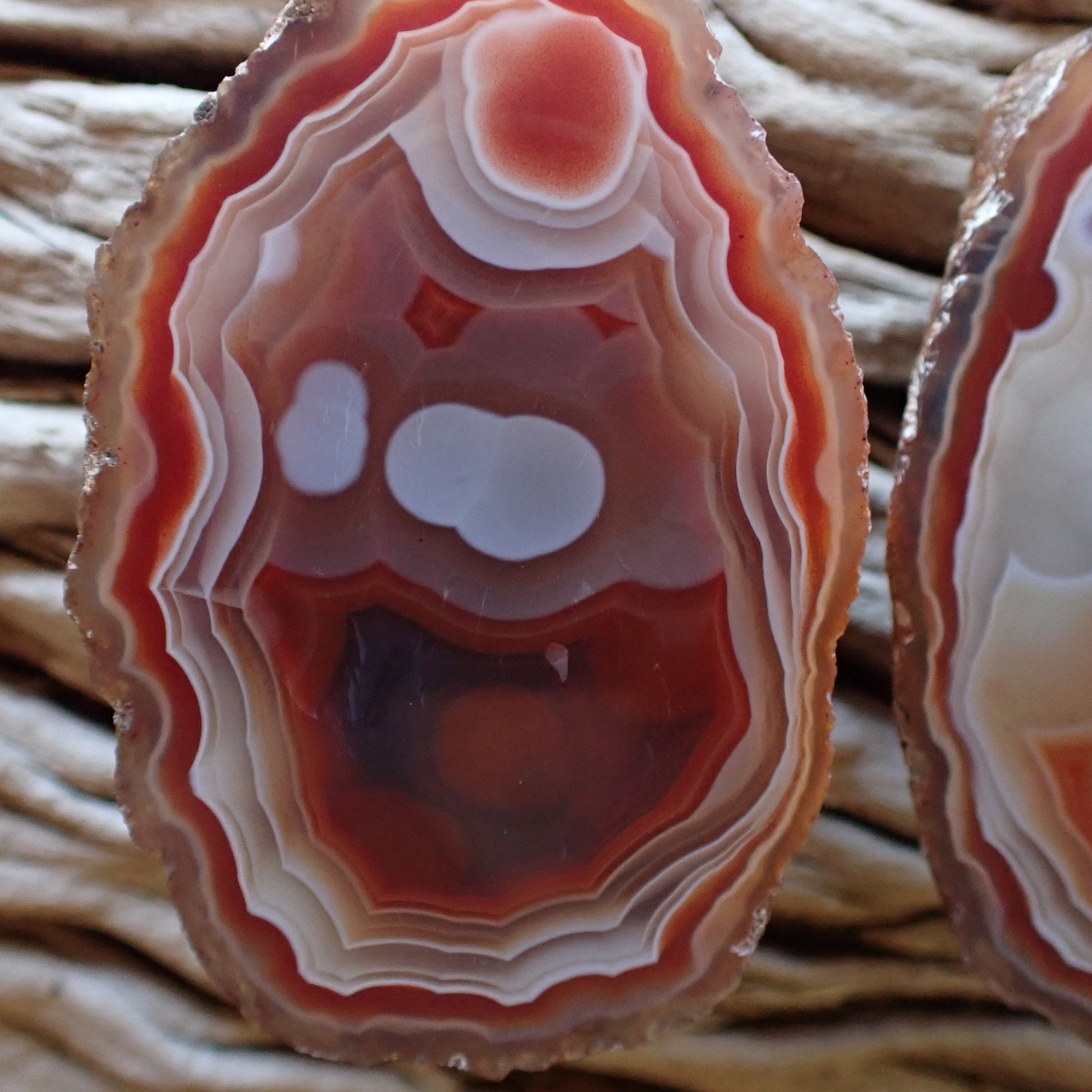 Macro detail of a Malawi agate specimen featuring unique pareidolia resembling a happy face, highlighted by tight micro-banding and deep carnelian red "smile" and eyes.