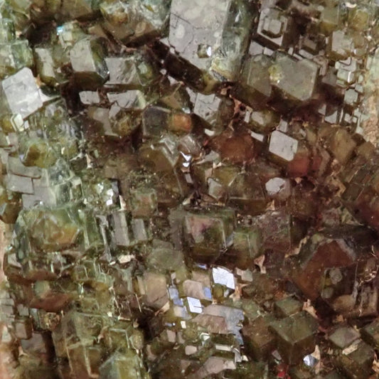 Demantoid garnet from Madagascar, close-up of olive-green andradite crystals showing reflective faces and stepped growth.