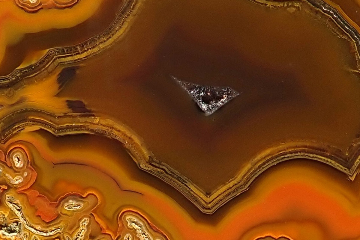 Lilangabi agate 68 mm – detail of fine fortification bands around brown chalcedony and a small drusy vug, with orange-yellow chromatography and moss inclusions.