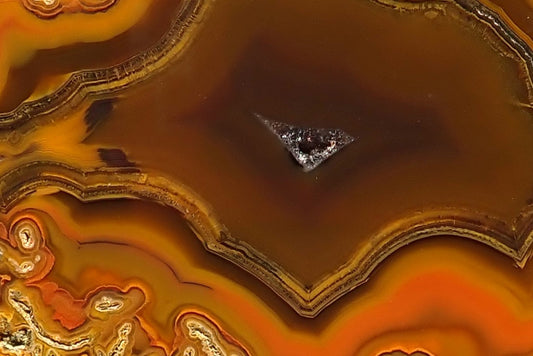 Lilangabi agate 68 mm – detail of fine fortification bands around brown chalcedony and a small drusy vug, with orange-yellow chromatography and moss inclusions.