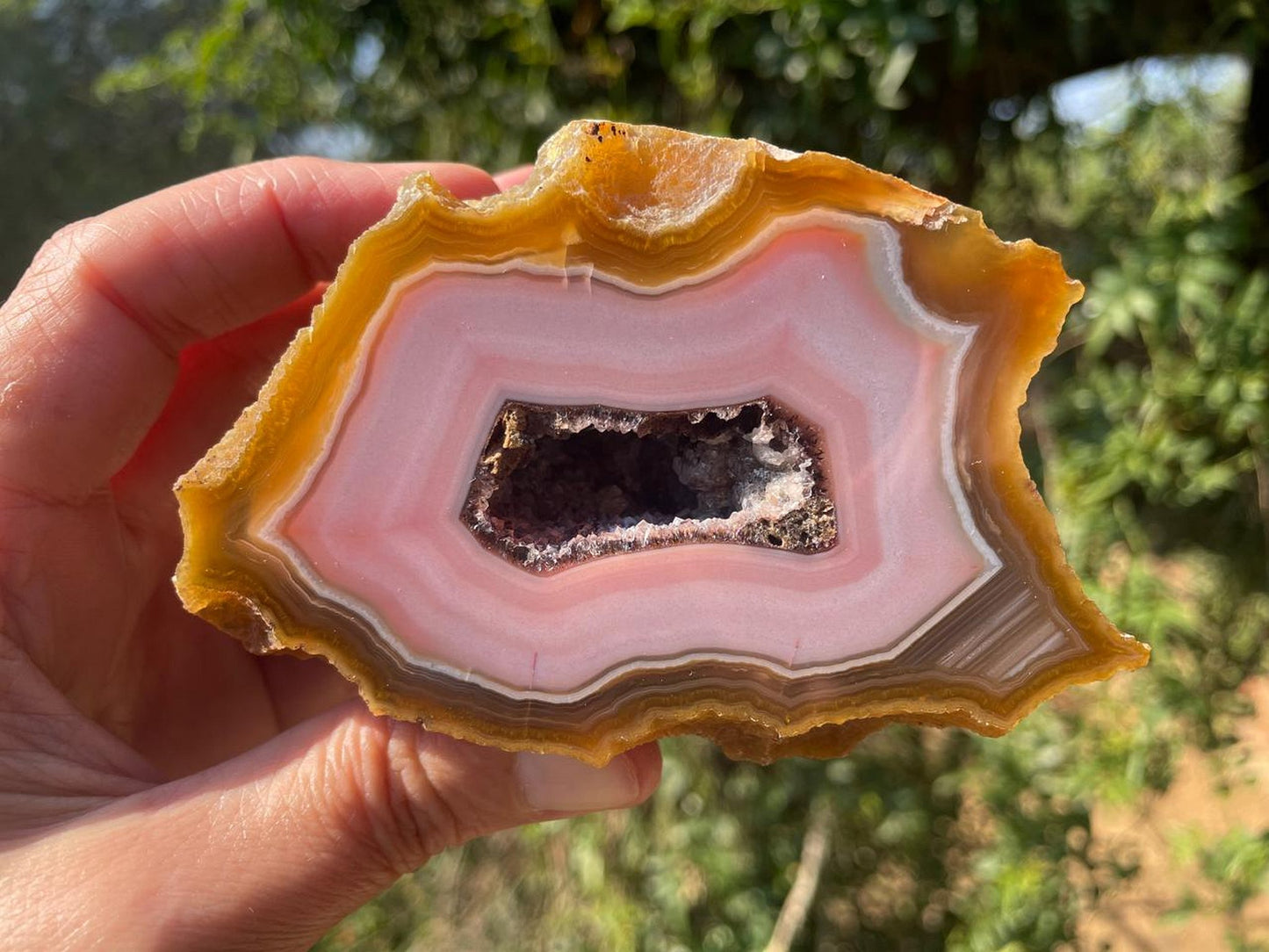Lilangabi agate 100 mm – in-hand view, druzy vug, pink chalcedony and amber banding, Eswatini | SKU LIL00026