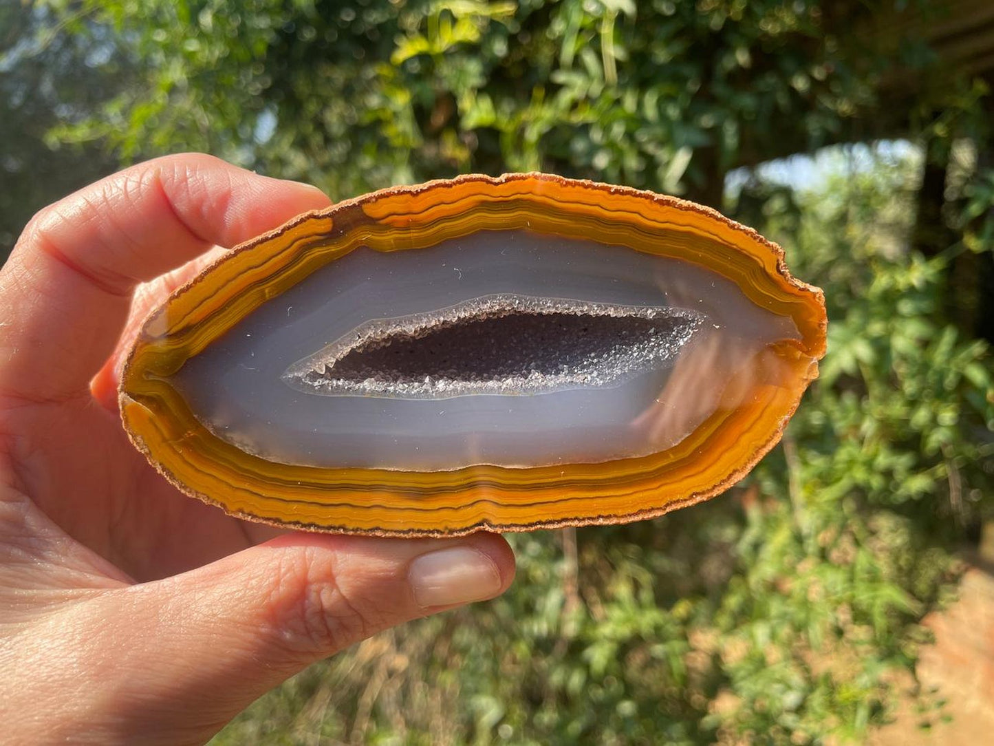 Lilangabi agate 107 mm – in-hand view, druzy vug, amber scalloped banding, blue-grey chalcedony, Eswatini