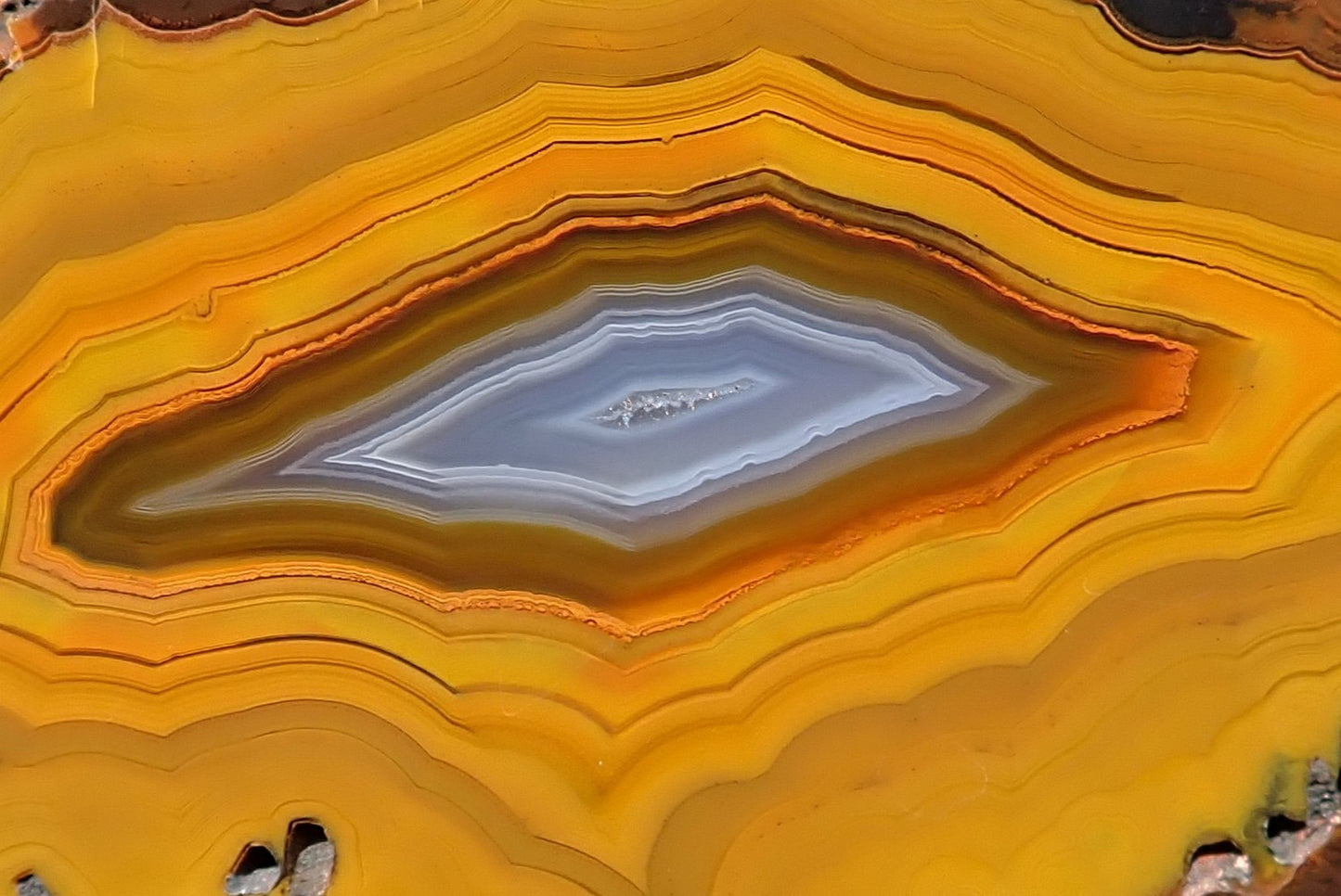 Lilangabi agate 87 mm – close-up, angular chevron banding, deep amber and burnt orange, blue-grey vug centre