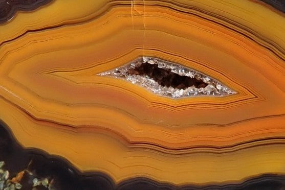Lilangabi agate 67 mm – face detail, chromatography banding, drusy vug with grey-white quartz crystals, burnt orange to near-black