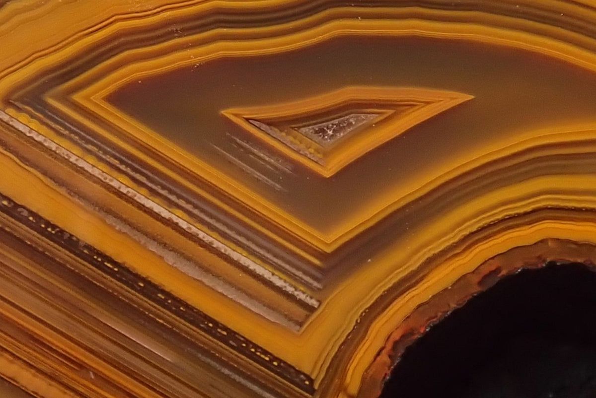 Lilangabi agate 102 mm – close-up of the chevron banding point, fine concentric fortification lines in amber and burnt gold, Lebombo Mountains