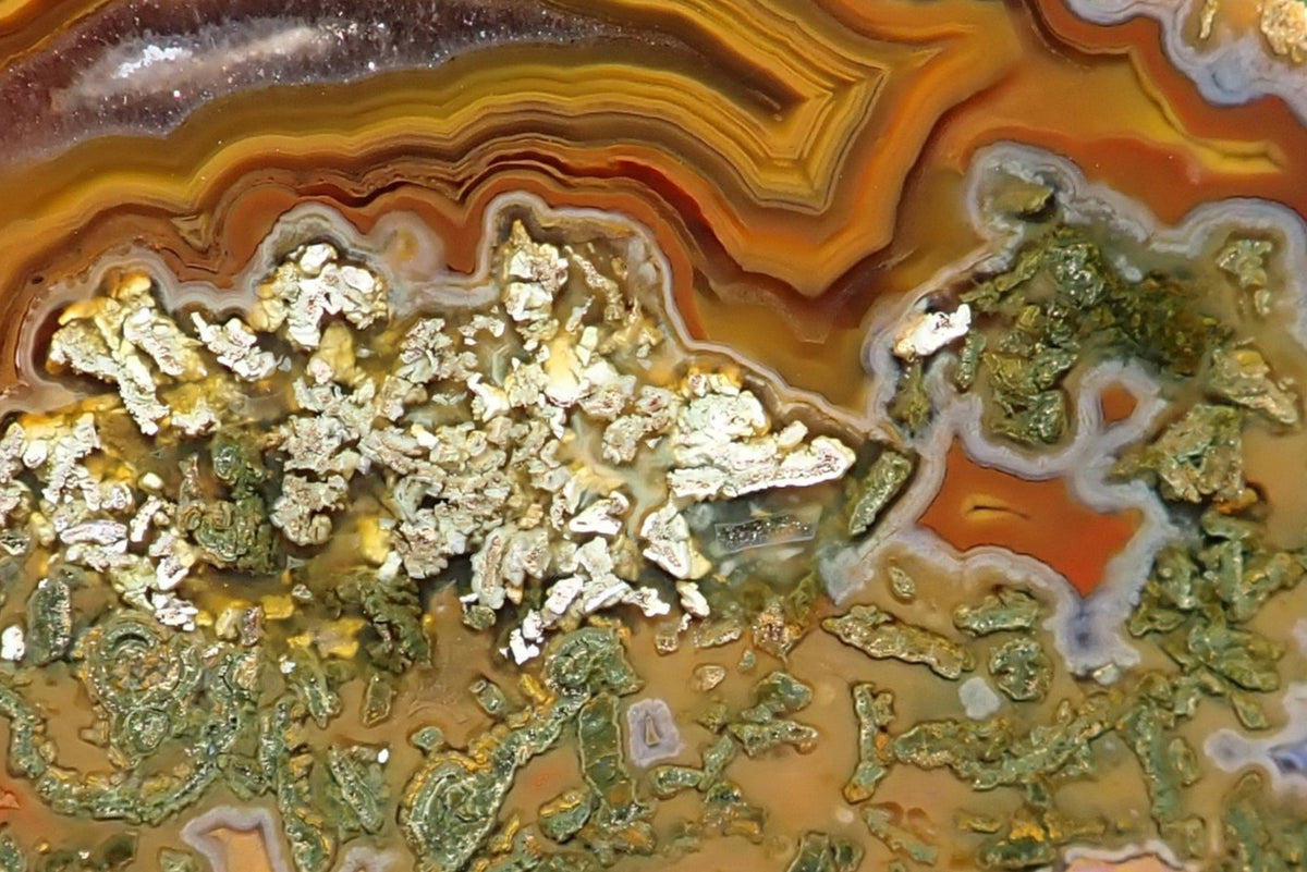 Lilangabi agate 72 mm, detail of chromatography and fortification banding bordered by pale grey bands, with green moss inclusions and small agate chambers below.
