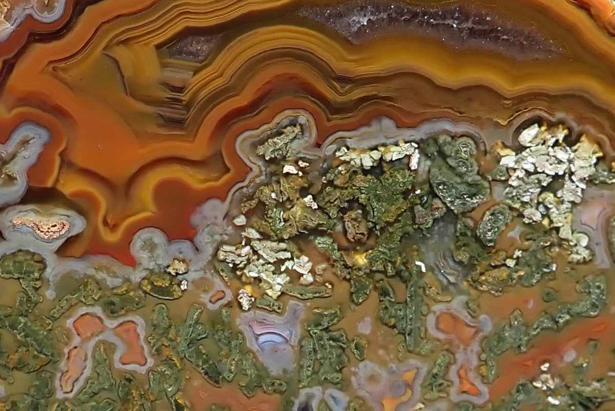Lilangabi agate 72 mm, detail of tightly layered yellow, amber and brown fortification banding, a smooth amethyst section, and pale grey bands bordering green moss inclusions and small agate chambers.