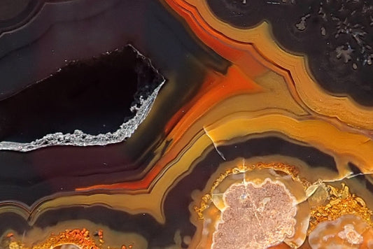 Lilangabi agate 71 mm, detail of the open vug and surrounding fortification bands, with charcoal-purple layers bordered by orange and golden yellow.