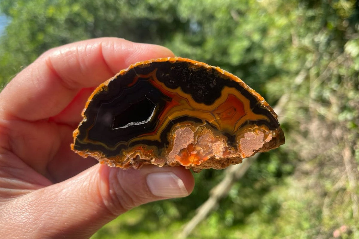  Lilangabi agate 71 mm held between fingers for scale, showing an open vug, fortification banding and pale cream-pink areas along the lower face.