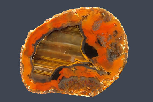 Lilangabi agate 73 mm – hand-lapped face with amber and cream waterlines, chromatography, curved charcoal-grey banding and a thin yellow border within a vivid orange surround.
