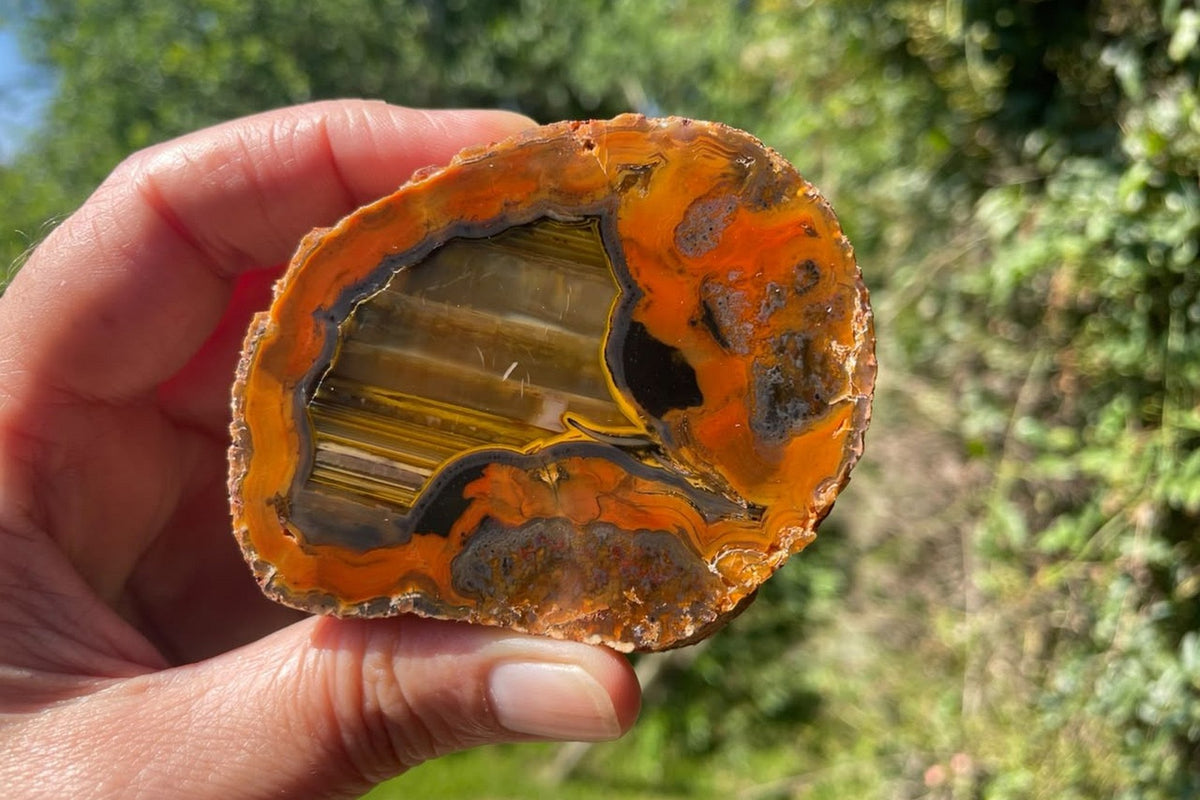 Lilangabi agate 73 mm – held for scale, showing horizontal waterlines, chromatography and charcoal-grey bands contrasting with the orange surround.