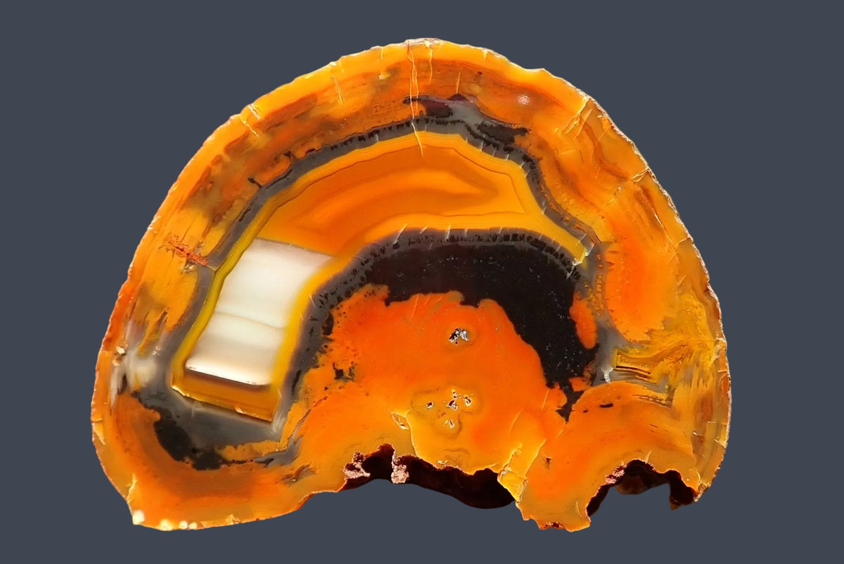 Lilangabi agate 60 mm – hand-lapped face with chromatography across orange-gold bands, broad cream-white waterlines on the left and curved charcoal-grey banding around the orange centre.