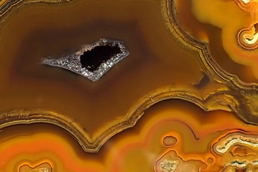 Lilangabi agate 71 mm – detail of the crystal-lined drusy vug in brown chalcedony, surrounded by fine angular bands and golden-yellow to orange chromatography.