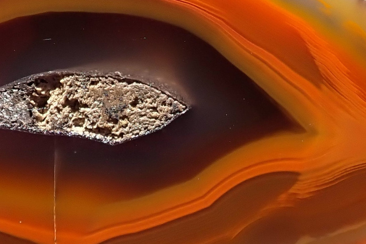 Lilangabi agate 68 mm – detail of the elongated central drusy vug, deep reddish-brown inner band and fine orange and amber layers showing chromatography.