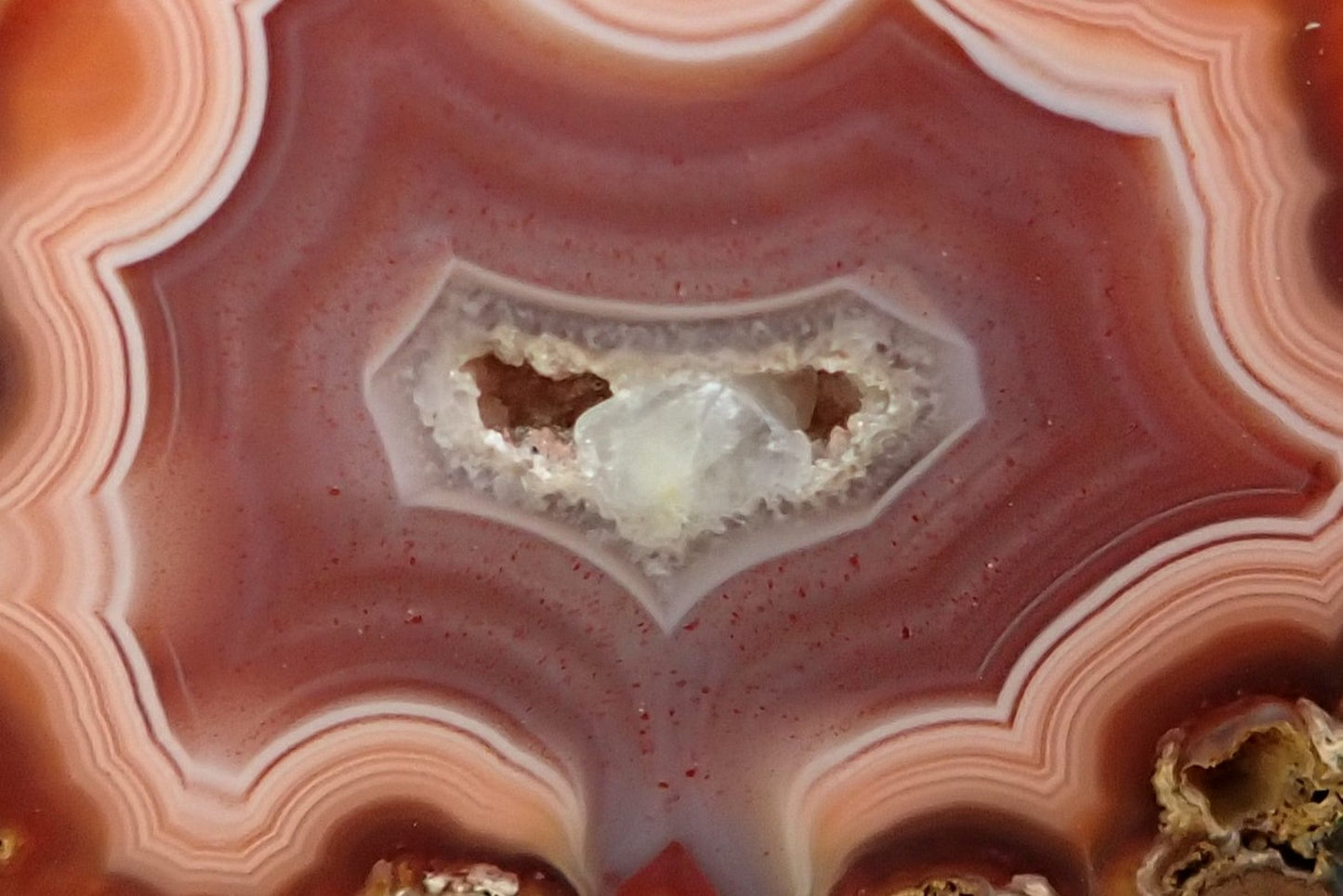 Malawi agate 40 mm – face detail, angular fortification bands, drusy vug with calcite crystal, burnt orange to rose-pink