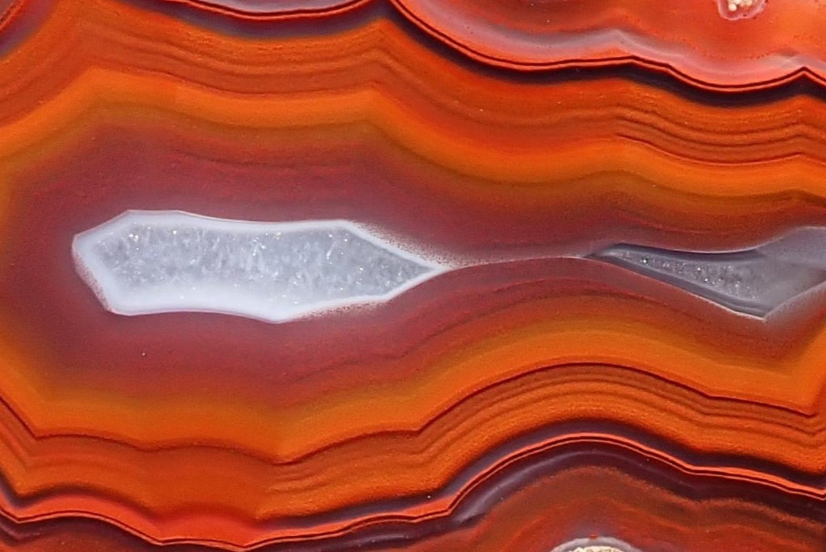 Malawi agate 57 mm, detail of two pale crystalline centres polished flat, surrounded by purple-grey layers and finely outlined orange-red fortification banding, Ngabu.
