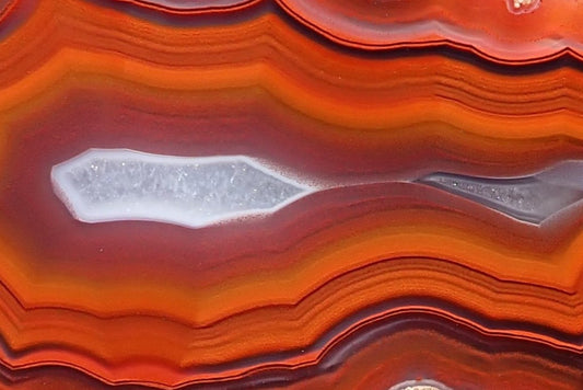 Malawi agate 57 mm, detail of two pale crystalline centres polished flat, surrounded by purple-grey layers and finely outlined orange-red fortification banding, Ngabu.