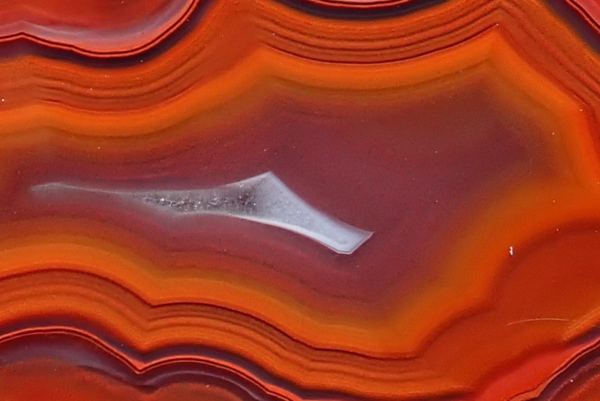 Malawi agate 55 mm, detail of the narrow pale crystalline section within the purple-grey centre, surrounded by finely layered orange-red fortification banding, Ngabu.