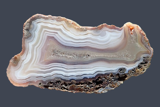 Malawi agate 66 mm, polished face with ghost banding among fine white, grey and pale mauve bands surrounding an elongated crystalline centre, Ngabu, Malawi.