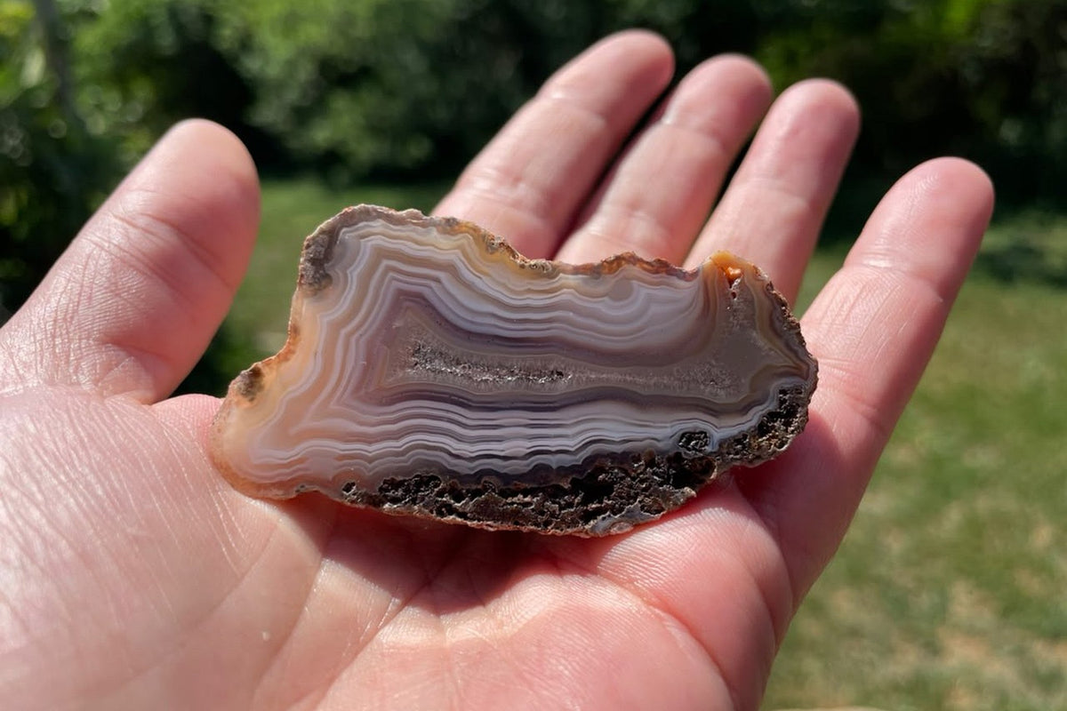 Malawi agate 66 mm resting in a palm for scale, showing ghost banding, an elongated crystalline centre and natural outer edge, Ngabu, Malawi.