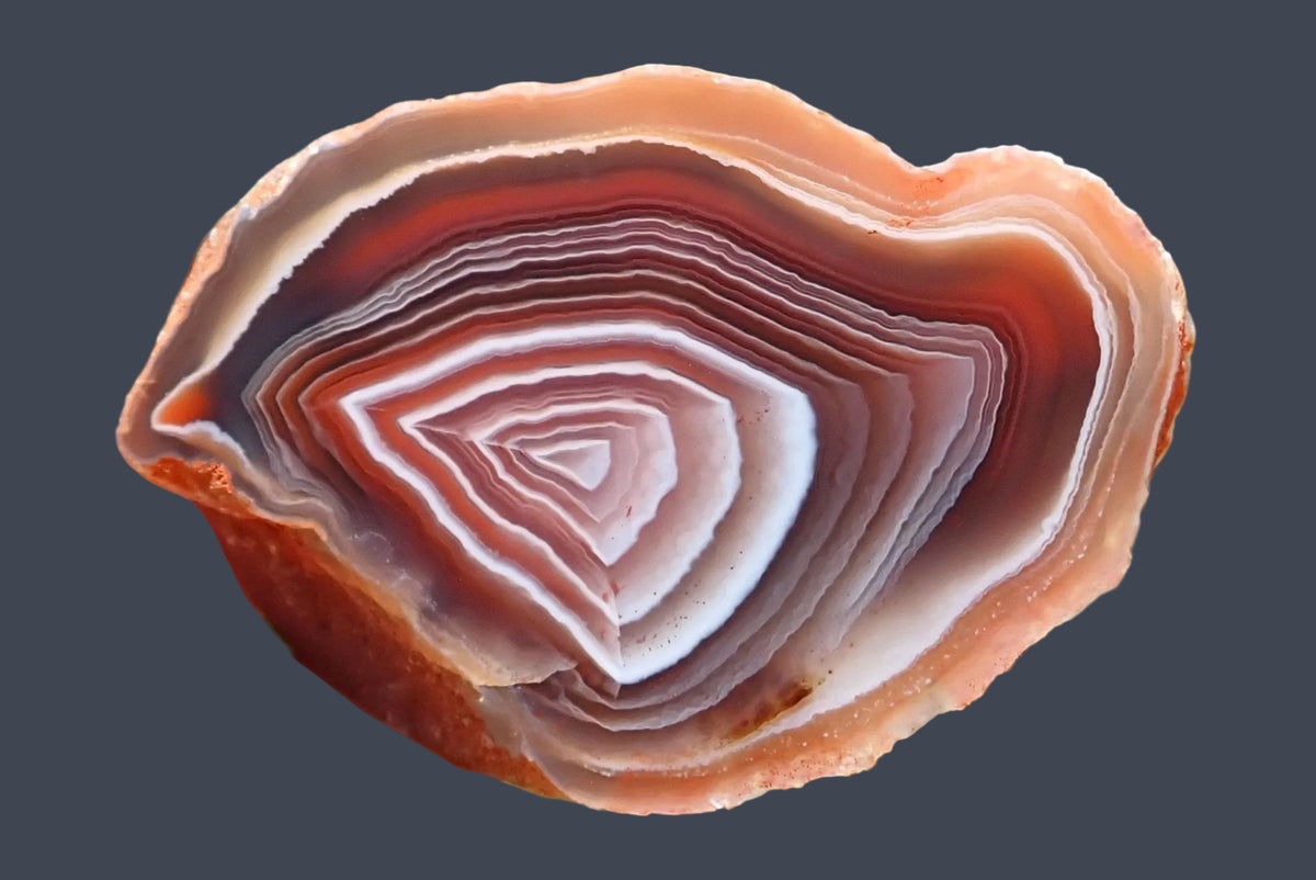 Mozambique agate 55 mm, also known as Swazi agate, showing angular white bands around a pale pink centre, fine ghost banding and chromatography through mauve-grey and reddish-orange layers.
