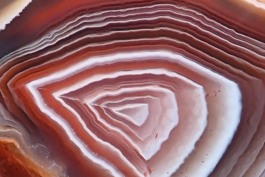 Mozambique agate 55 mm, face detail showing fine ghost bands between broader white layers, with dusty pink, mauve-grey and reddish-orange chromatography.