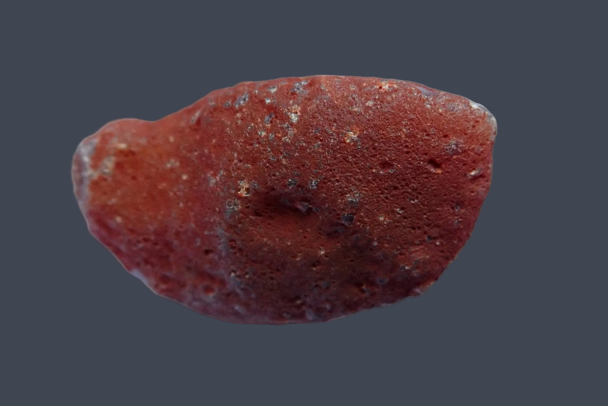 Mozambique agate 55 mm, back view showing the unpolished reddish-brown natural surface with small pits and scattered grey patches.