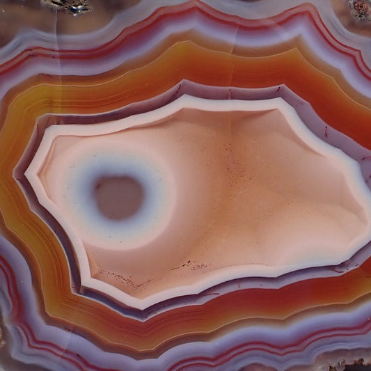 close up detail of malawi agate with stunning orange red and purple banding with an eye in a peach centre